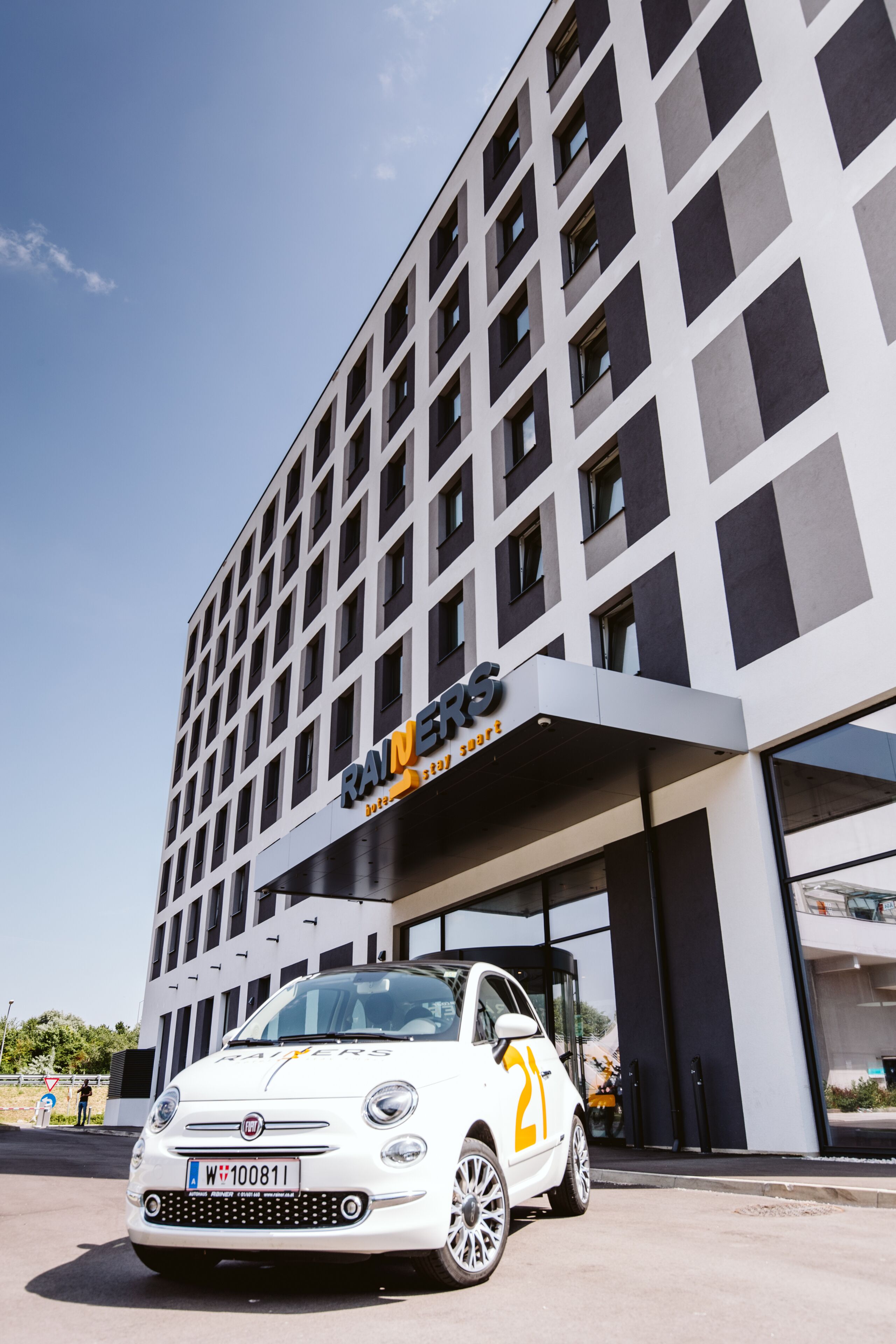 Ein modernes Gebäude mit weißer Fassade und einem geparkten Auto davor.