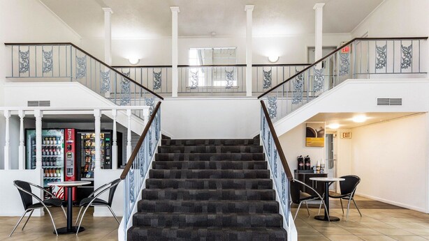 A staircase with a dark carpeted landing and white balustrades, leading to a second-floor area with a Coca-Cola vending machine and a small table with chairs. - Studio 6 Alexandria, LA (Alexandria)