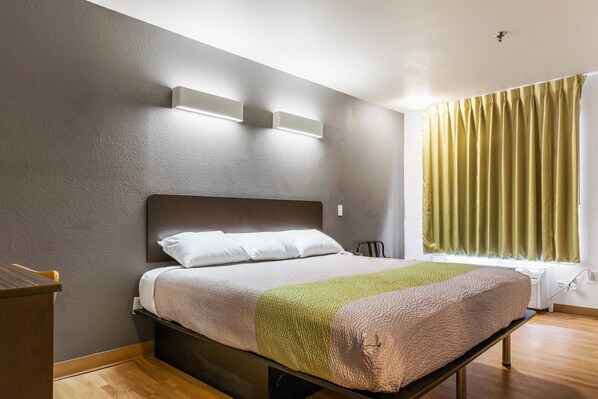 Un dormitorio con una cama, una mesita de noche, una ventana con cortinas y una lámpara de pared.