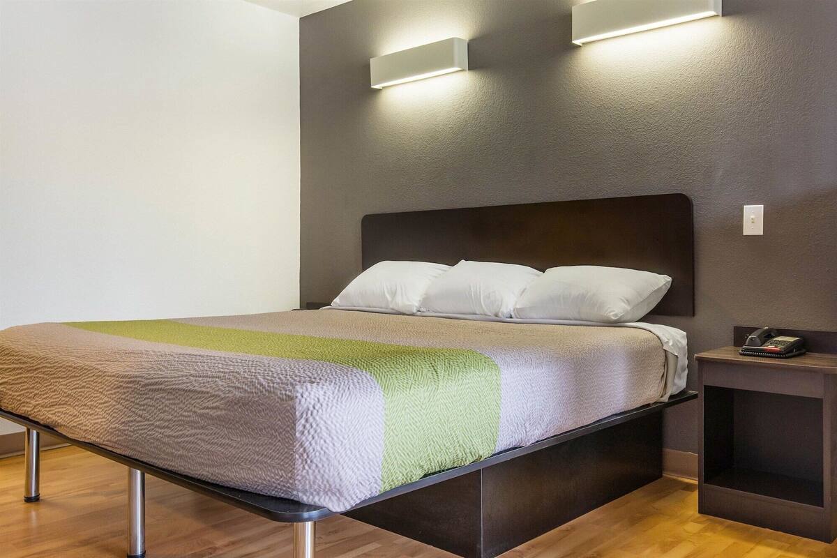 A modern hotel room with a bed, a nightstand, and a wall-mounted light fixture.