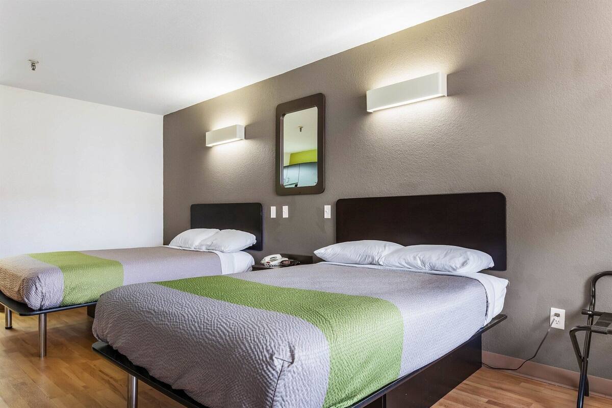 A hotel room with two beds, a mirror, and a wall-mounted light fixture.