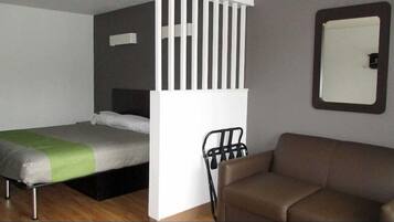 A compact room with a bed, a small sofa, and a mirror on the wall.
