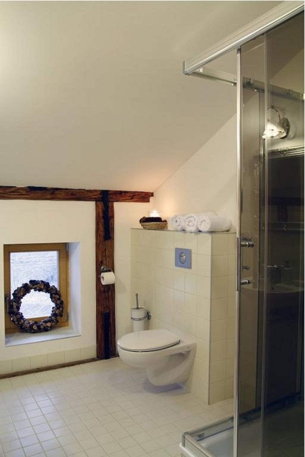 Ein Badezimmer mit Toilette, einer Duschkabine aus Glas, einem Handtuchhalter und einem Fenster mit einem Kranz.