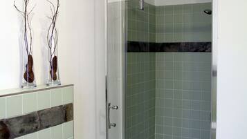 Ein Badezimmer mit einer Glaskabine zur Dusche, gefliesten Wänden und einem Holzregal mit Dekoration.