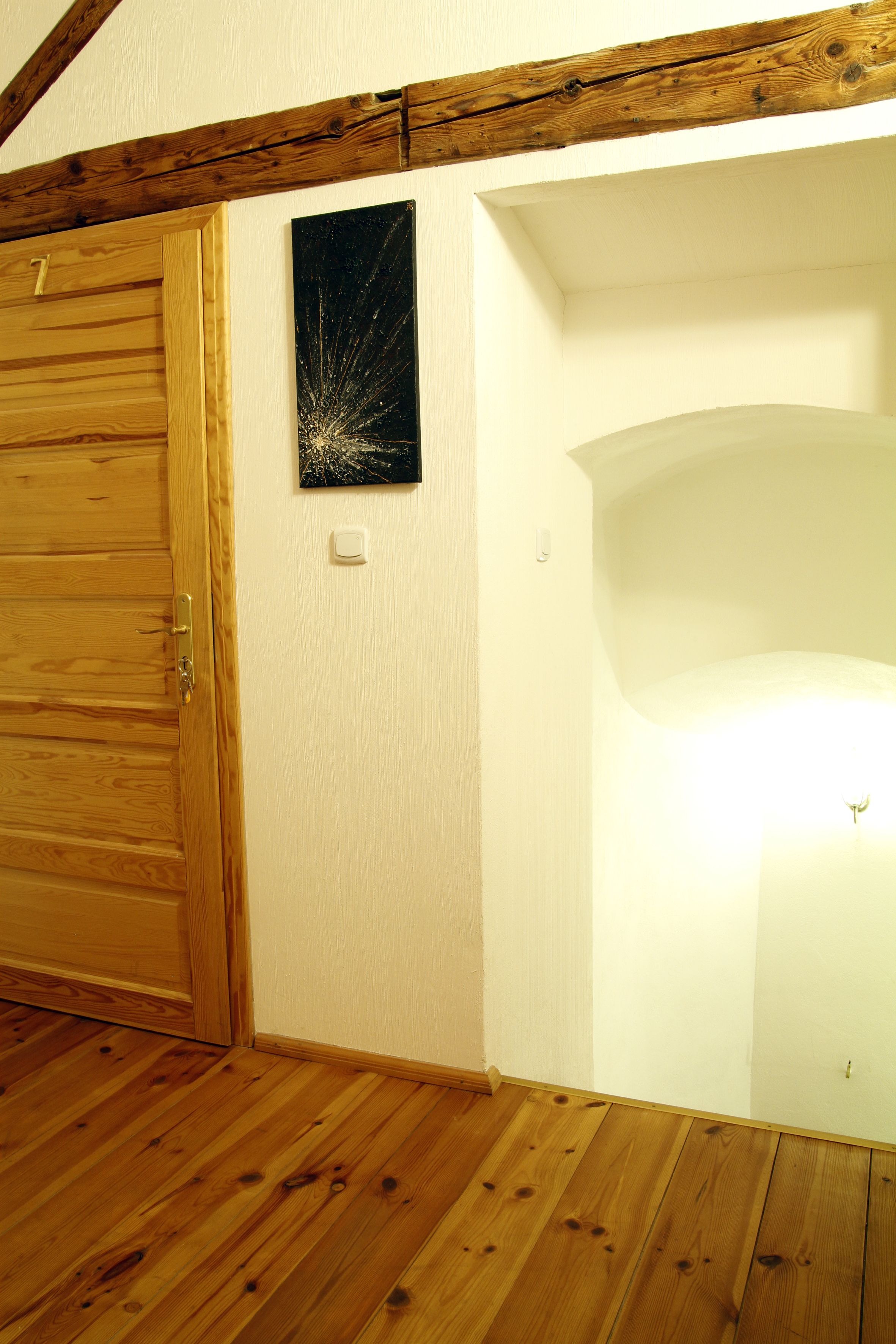 A wooden door with a number, a white wall with a picture, and a white ceiling.