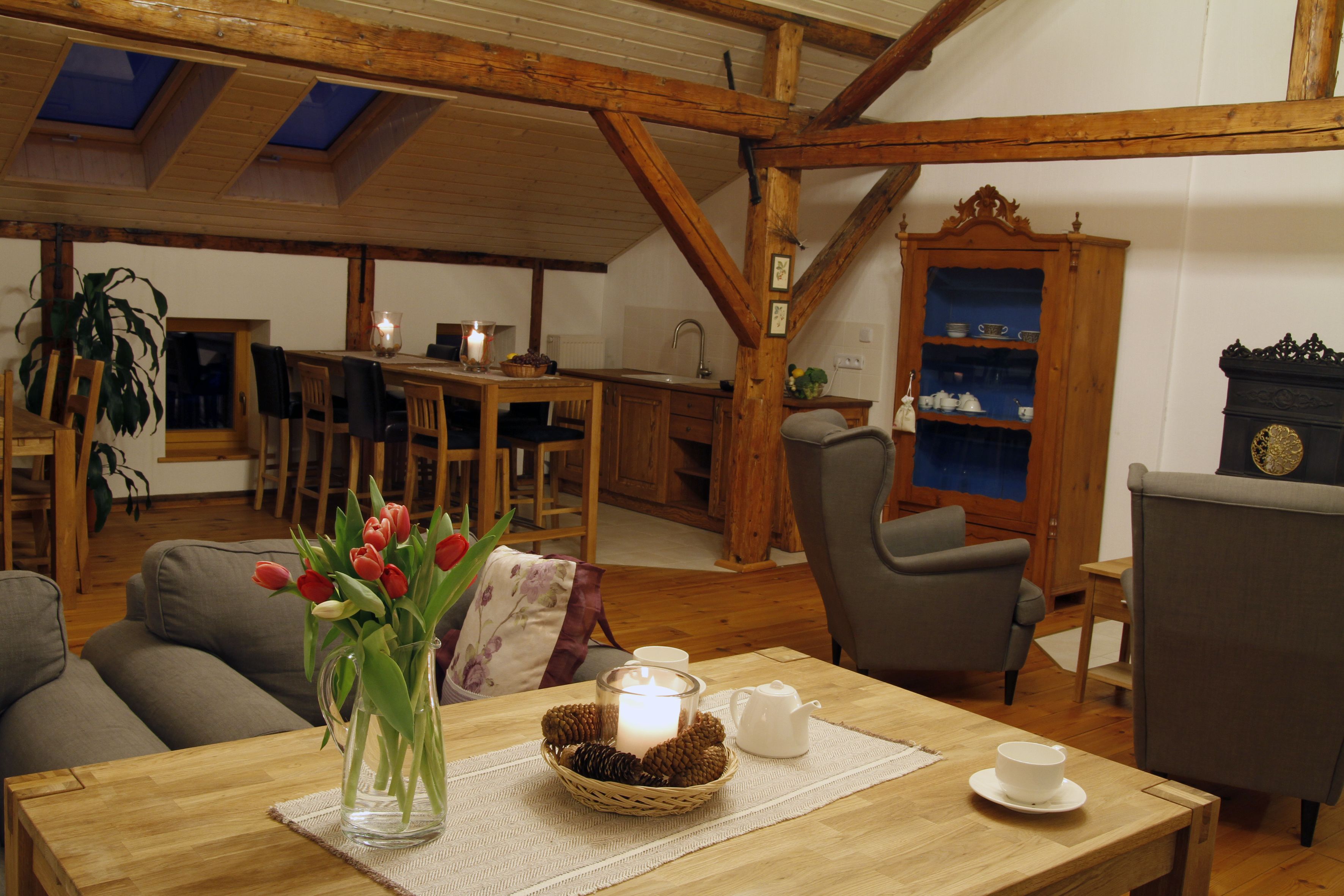 A cozy living room with a wooden table, a vase of tulips, a lit candle, and a rustic wooden cabinet.