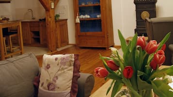 Een gezellige woonkamer met een houten plafond, een kroonluchter, een bank met bloemenkussens en een vaas rode tulpen op een houten tafel.
