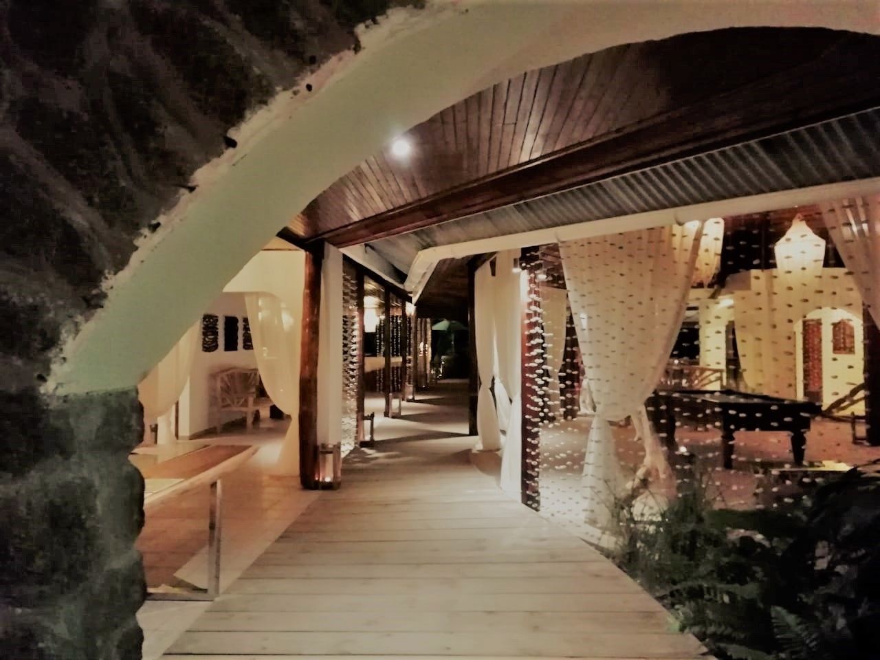 A corridor with wooden flooring, white curtains, and a brick wall.