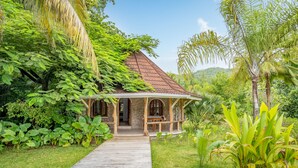 A wooden pathway leading to a house with a tiled roof, surrounded by lush greenery and palm trees. - Bliss Hotel Praslin (Praslin Island)