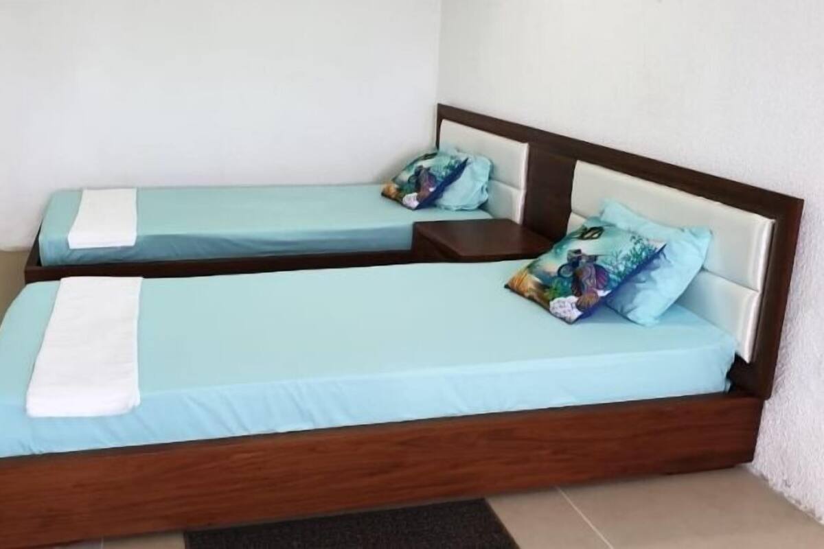 Dos camas individuales con ropa de cama azul claro a juego y cabeceros de madera, cada una con una almohada y una mesita de noche.