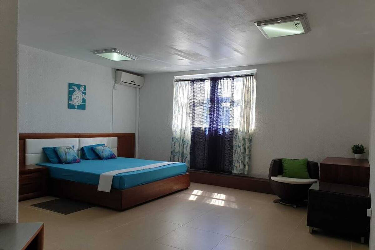 Un dormitorio con cama, escritorio, silla, ventana con cortinas y aire acondicionado.