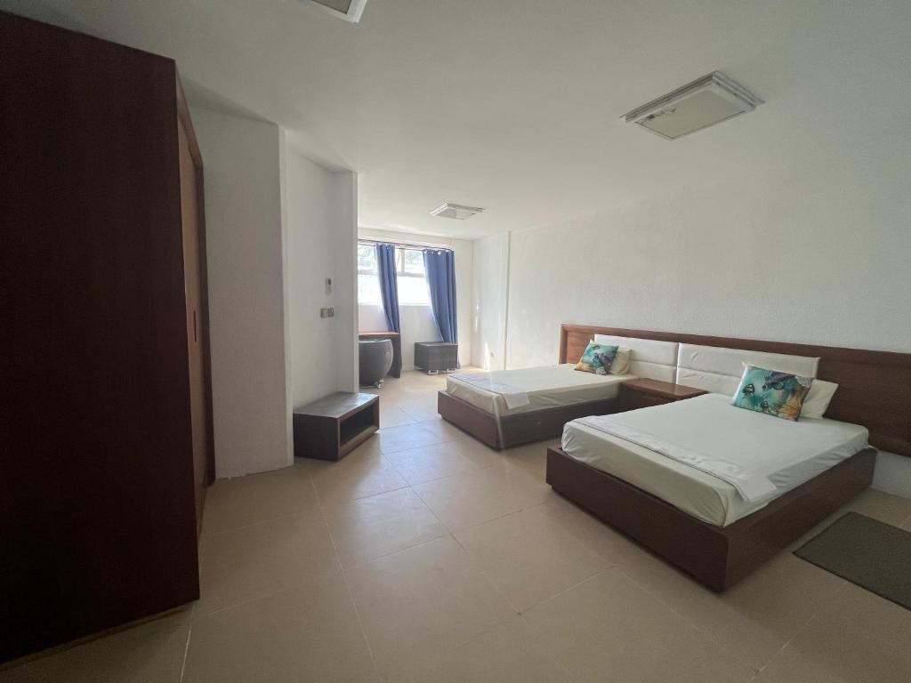 A hotel room with two beds, a wardrobe, a small seating area, and a view of the outside.