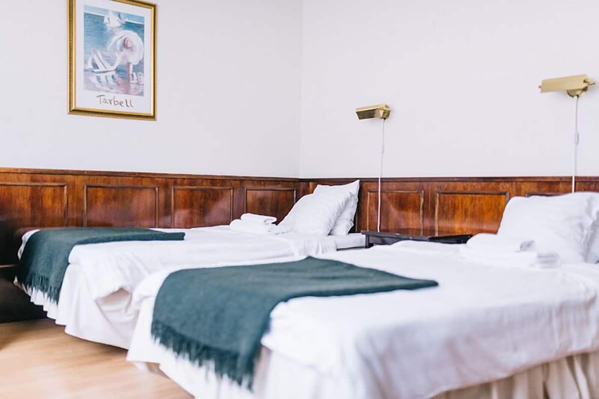 A hotel room with three single beds, wooden headboards, white bedding, and a framed picture on the wall.