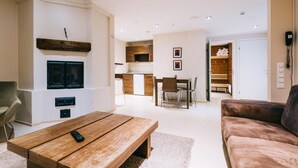 A modern living room with a wooden coffee table, a brown sofa, and a TV mounted on the wall. There is a dining area with a table and chairs, and a kitchen in the background. - Comfort Guesthouse (Jakobstad)