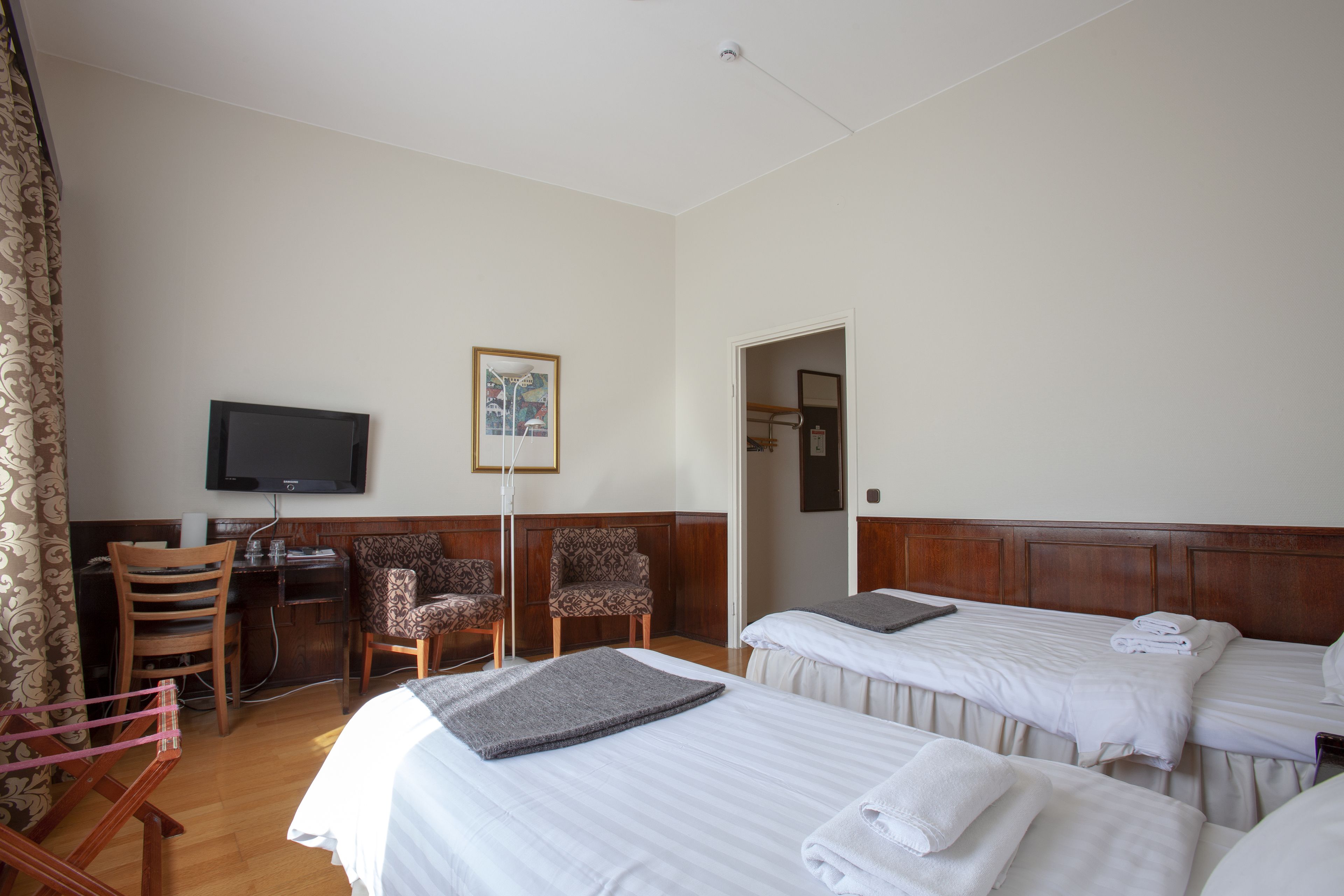Habitación de hotel con dos camas, un escritorio, una silla, un televisor y un cuadro en la pared.