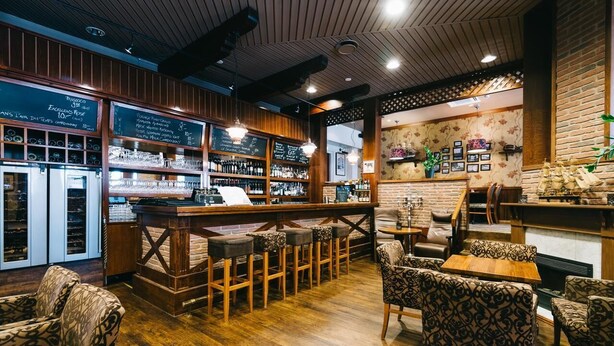 A cozy bar area with wooden furniture, a bar counter, and shelves stocked with bottles. - Comfort Guesthouse (Jakobstad)