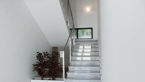 Una escalera moderna con escalones de mármol y barandilla, que conduce a una plataforma con una planta en maceta y un cartel que indica el nivel del piso.