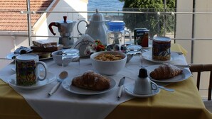 Una mesa en el balcón con comida para el desayuno y vista al mar.