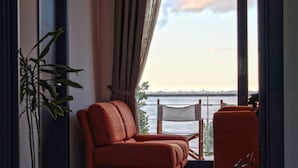 Una habitación con sofá y sillón orientados hacia un ventanal con vista a una masa de agua.