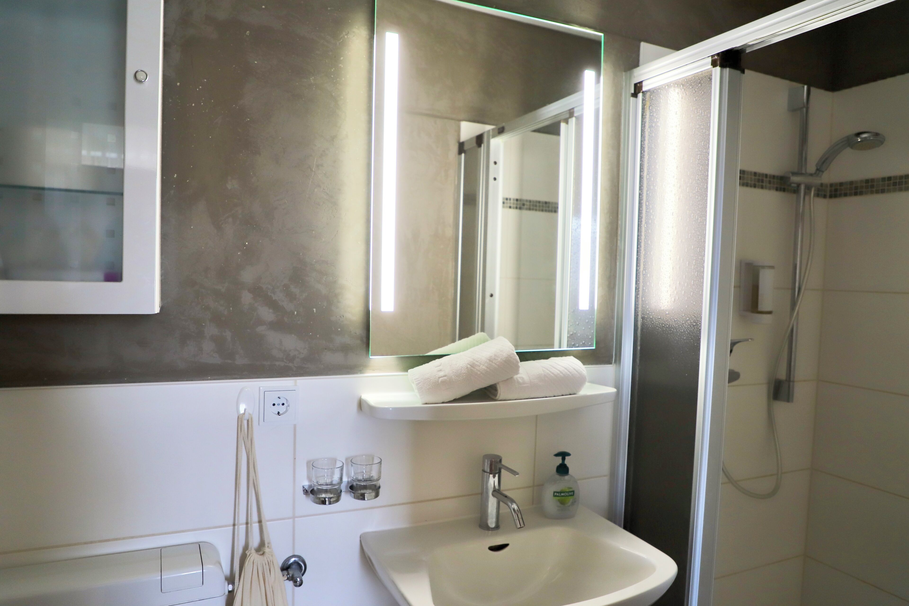 A bathroom with a sink, mirror, towel rack, and a shower area.