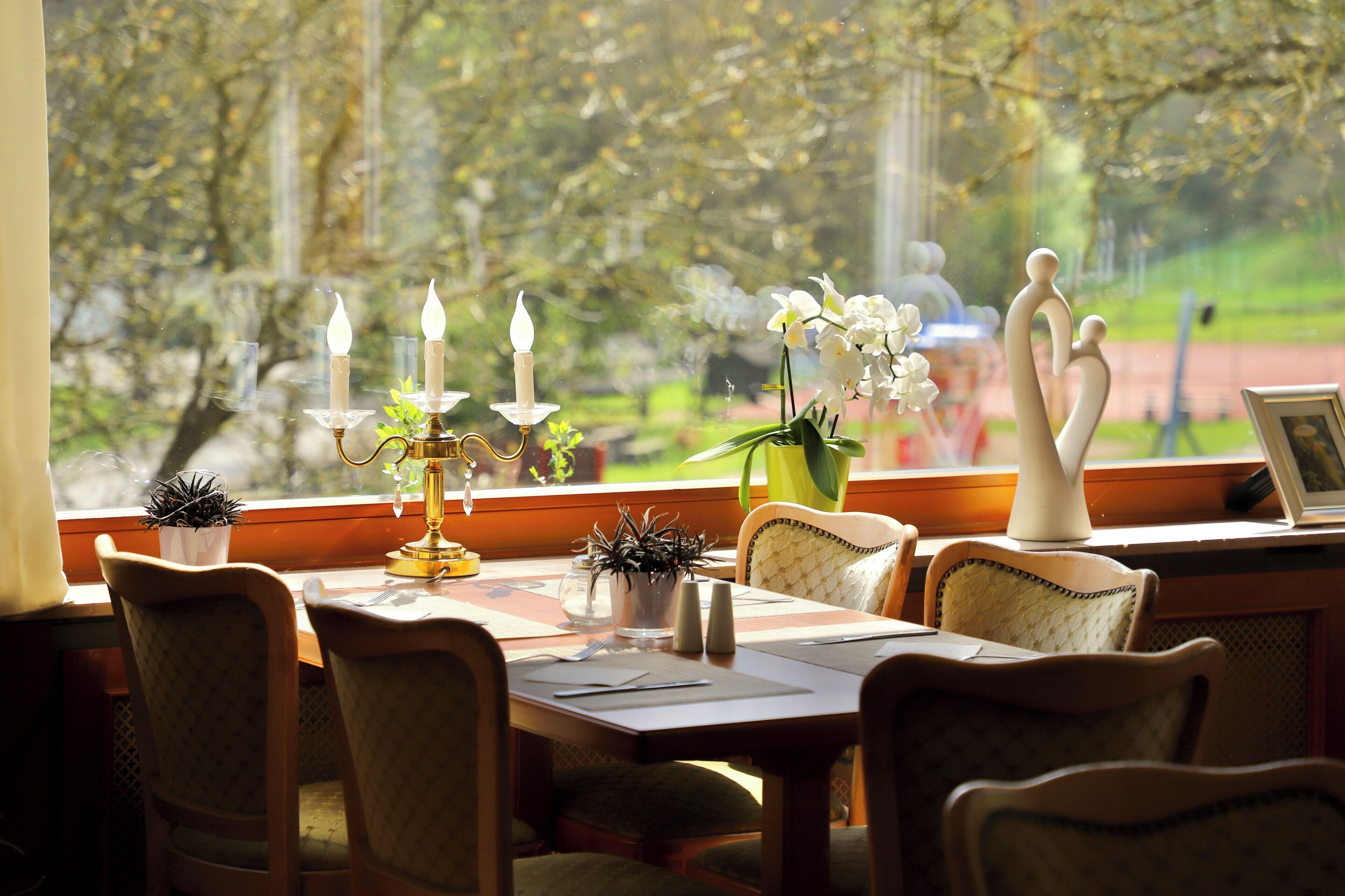 Un comedor con una mesa dispuesta para dos personas, que incluye un candelabro, un florero con flores y una figura decorativa.