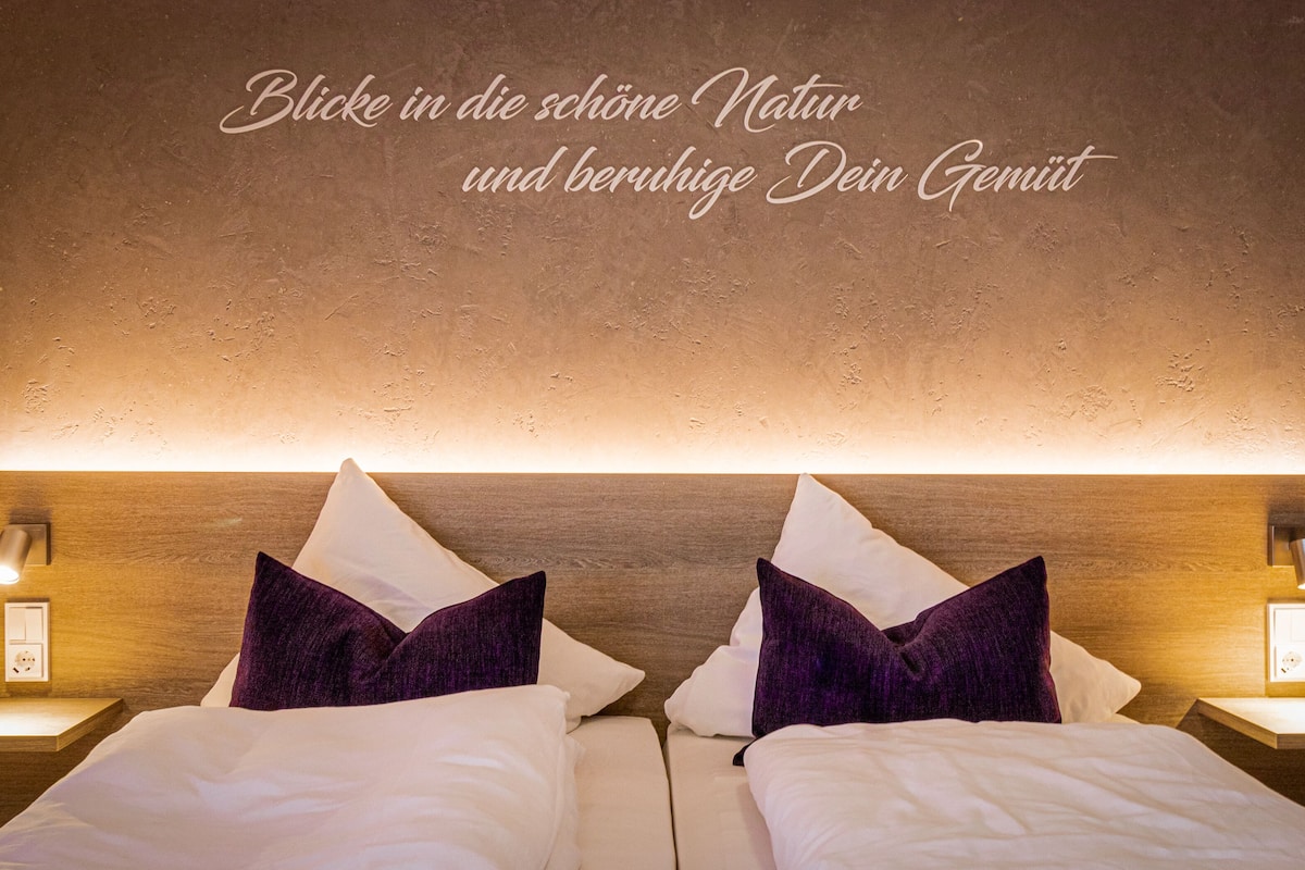 A hotel room with two beds, a wooden headboard, and a wall-mounted light fixture.