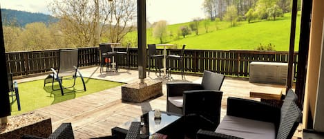 An outdoor patio with wicker furniture, a wooden deck, and a view of a green field.
