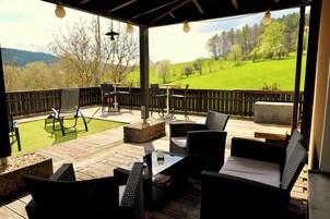 Un patio al aire libre con mobiliario de mimbre, una terraza de madera y vistas a un campo verde.