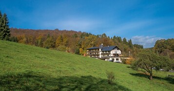A multi-story hotel with a sloped roof, situated on a grassy hillside with a forested backdrop.