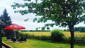Un espace extérieur verdoyant avec un parasol rouge, une table et des chaises.