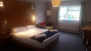 Une chambre d’hôtel avec un lit, une chaise, un bureau, une fenêtre avec des rideaux et un radiateur.
