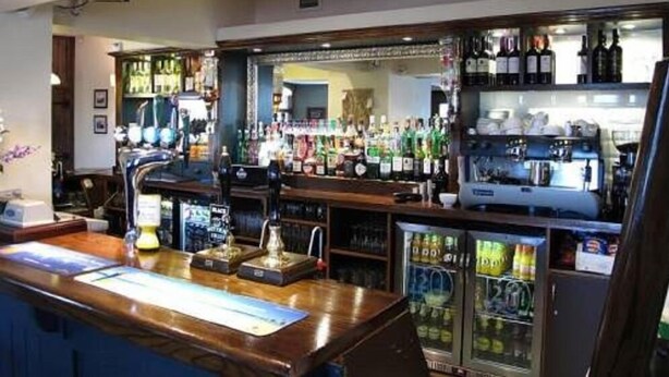 Un bar avec un comptoir en bois, des étagères remplies de bouteilles d ’alcool, un appareil à café et un réfrigérateur bien garni de boissons.