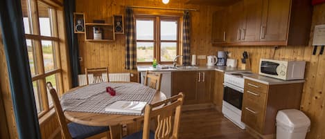 A wooden cabin kitchen with a dining table, chairs, a sink, a stove, and a microwave.