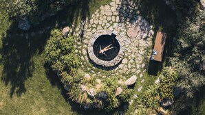 Une vue aérienne d’un chemin circulaire en pierre, avec un foyer central, entouré d’une végétation luxuriante et d’un banc en bois.