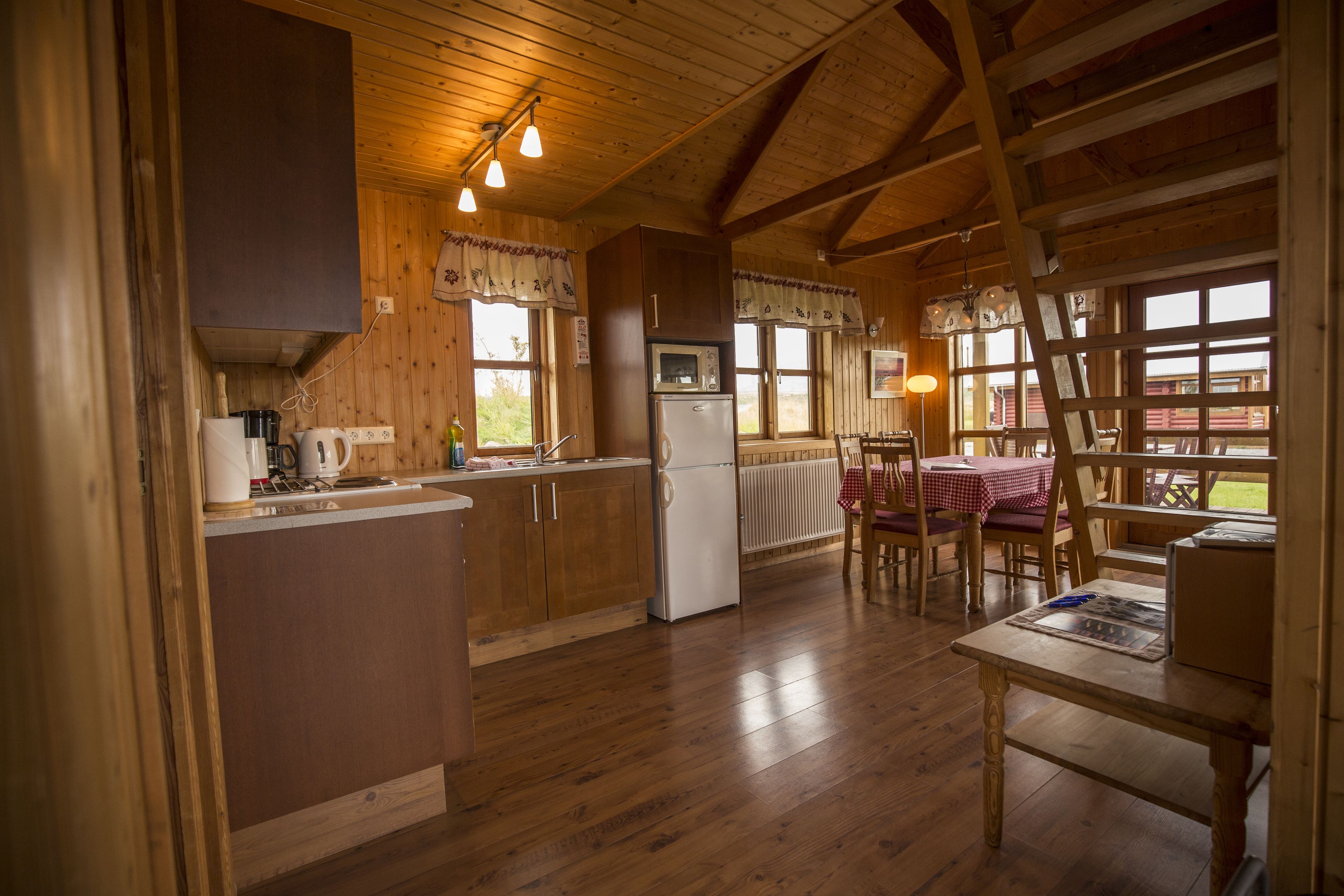 A wooden cabin interior with a kitchen, dining area, and a large window.