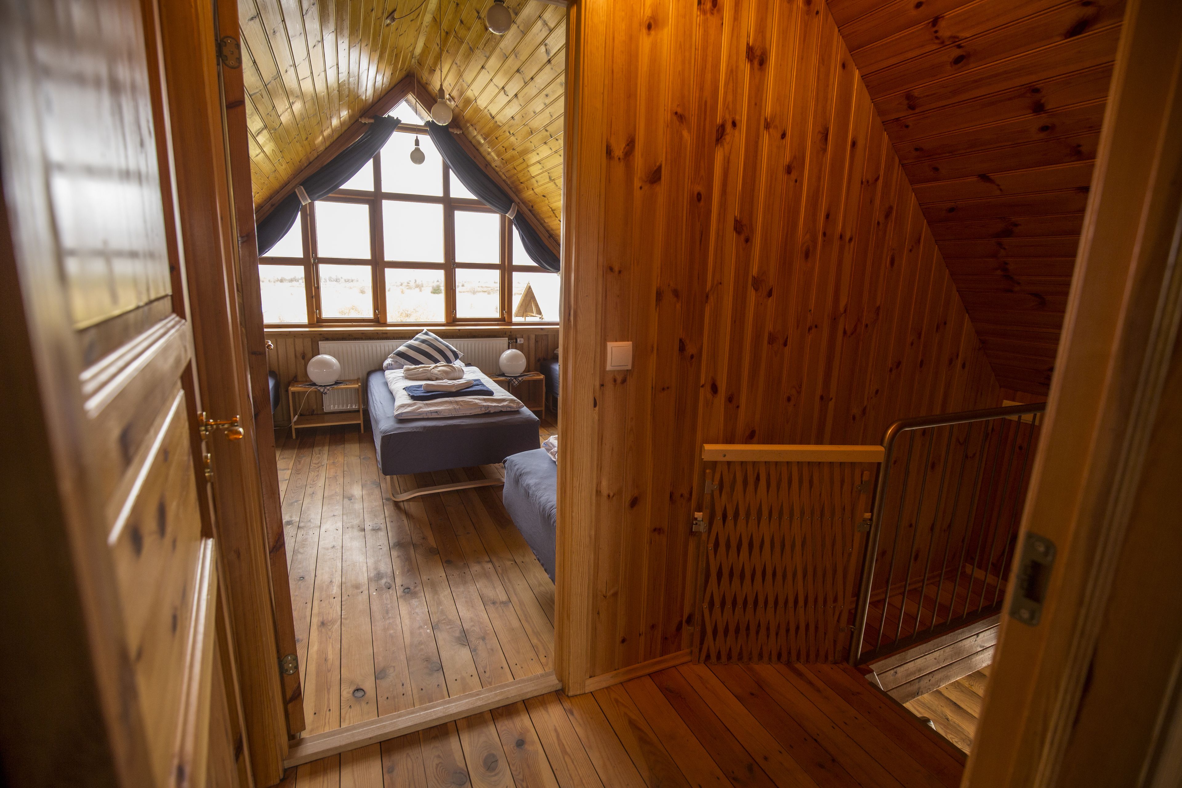 Une chambre mansardée en bois, avec un plafond en pente, un lit, une fenêtre et une petite table.