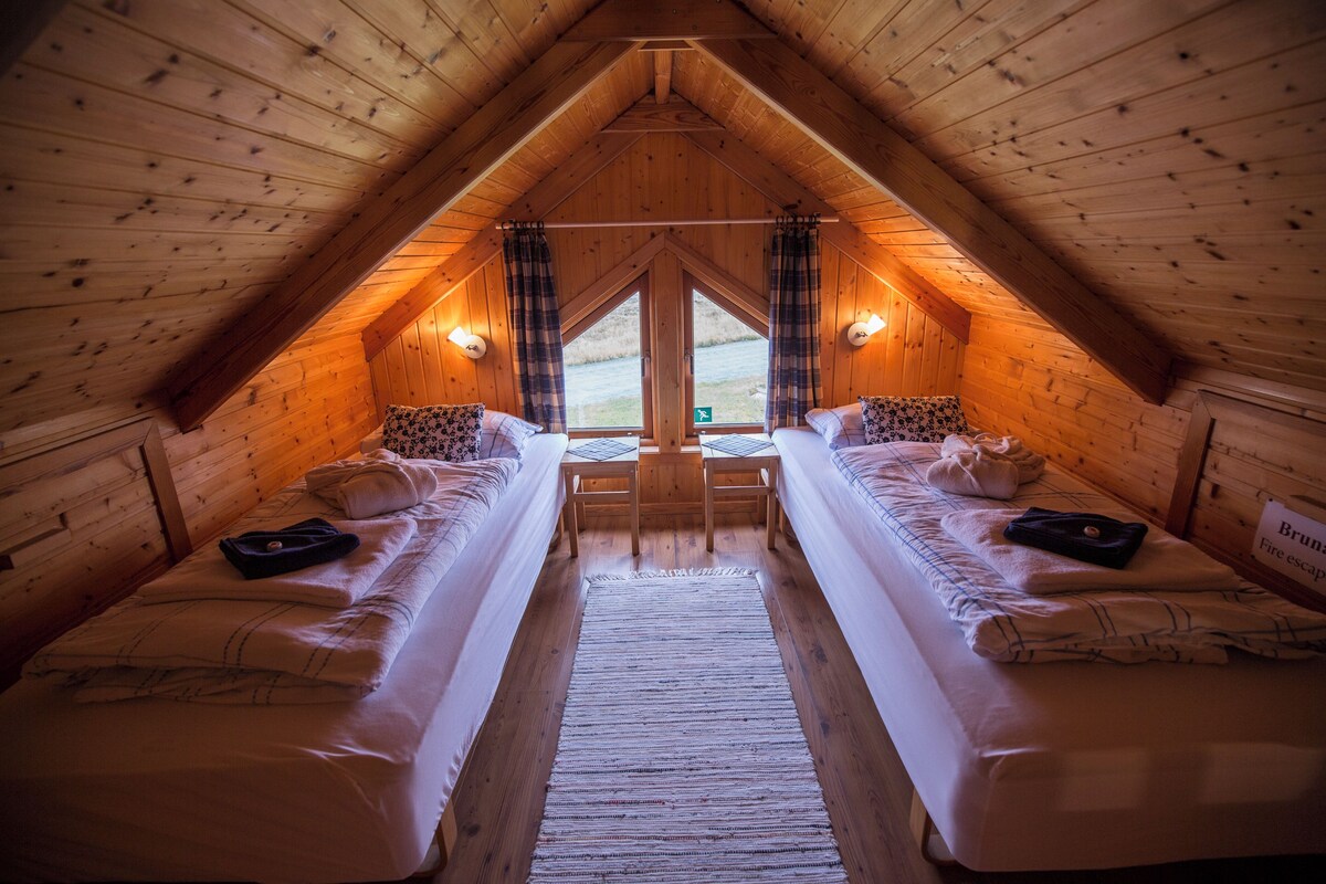 Une chambre confortable située sous les toits, avec deux lits, un plafond en bois et une vue sur l’extérieur.
