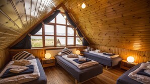 Un chalet confortable avec trois lits disposés en forme de U, des murs en bois et de grandes fenêtres offrant une vue sur l’extérieur.
