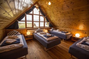 A cozy cabin with three beds arranged in a U-shape, wooden walls, and large windows offering a view of the outdoors.