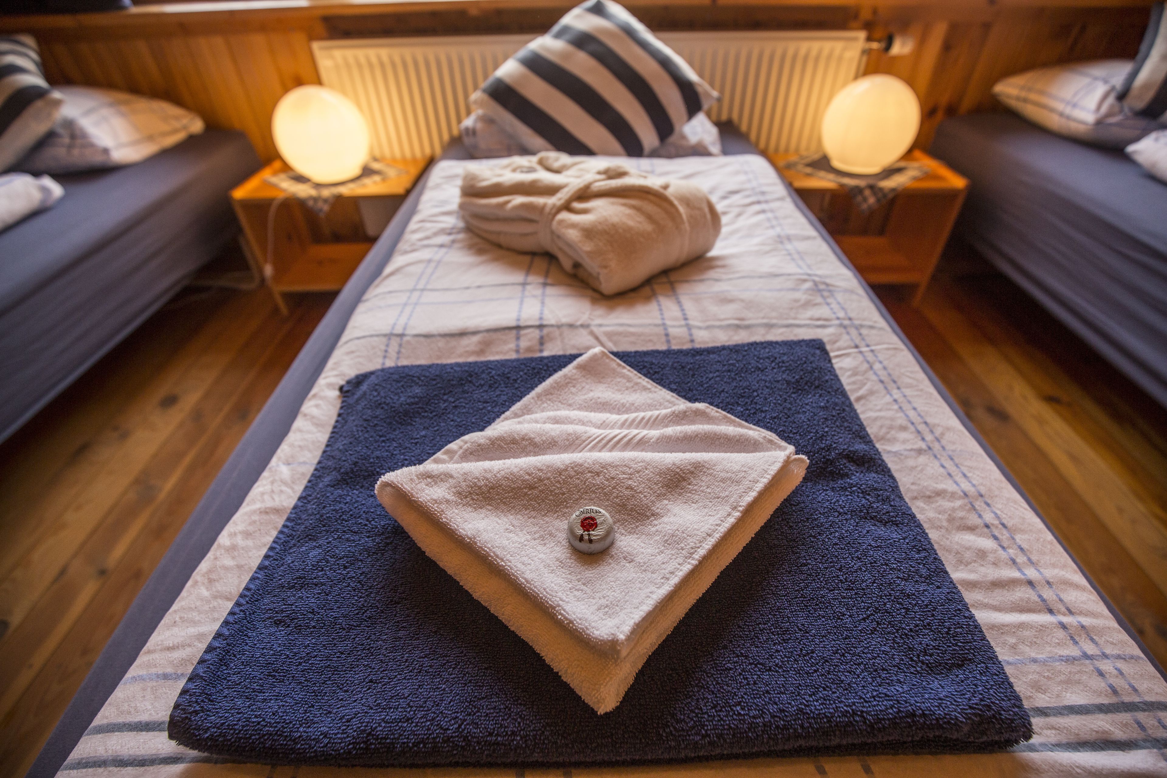 A neatly made bed with a folded towel and a small bottle, flanked by two bedside lamps on wooden nightstands.
