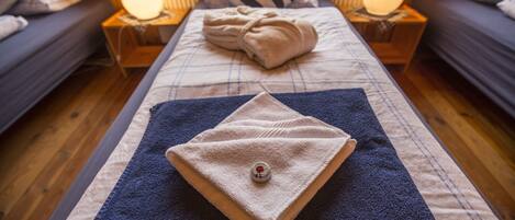 A neatly made bed with a folded towel and a small bottle, flanked by two bedside lamps on wooden nightstands.