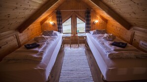 A cozy attic bedroom with two single beds, a wooden ceiling, and a view of the outdoors through a window.