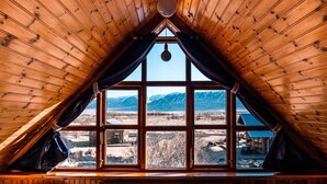Une pièce dotée d’un plafond en bois incliné et de grandes fenêtres offrant une vue sur les montagnes et un chalet.