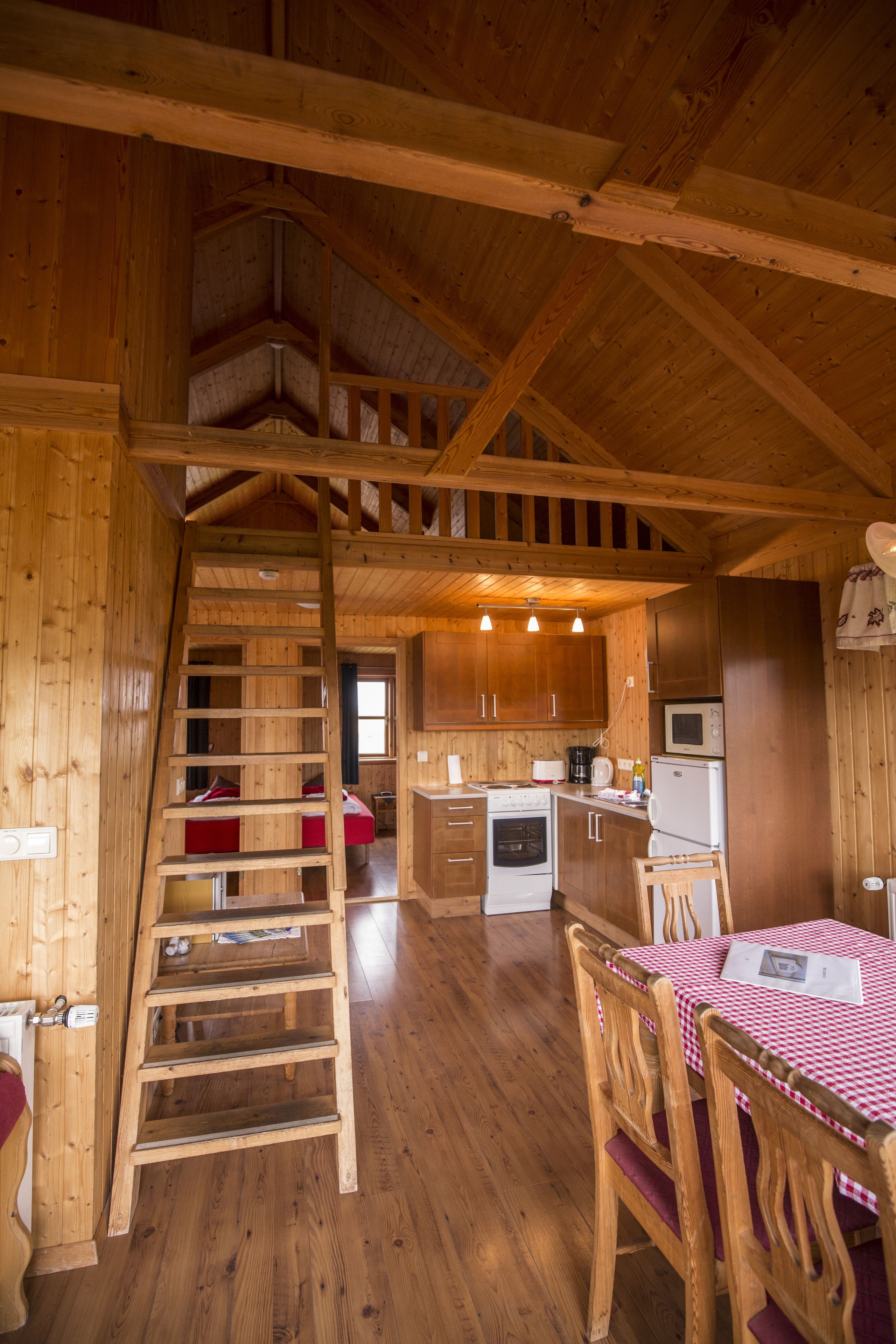 A wooden interior with a kitchen area, a dining table with chairs, and a wooden staircase.