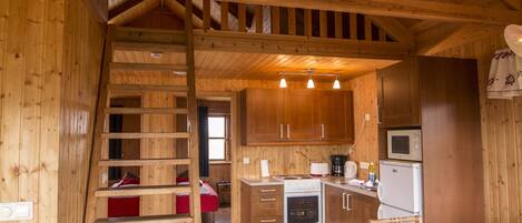 A wooden interior with a kitchen area, a dining table with chairs, and a wooden staircase.