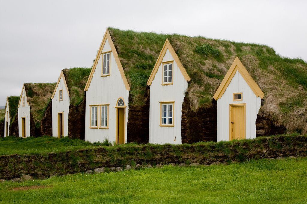 Une rangée de maisons blanches aux bordures jaunes, construites sur une colline verdoyante, avec un mur de pierres en façade.