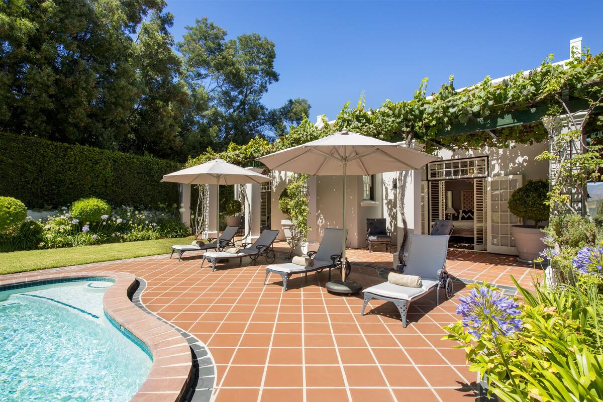 A poolside area with tiled flooring, lounge chairs, umbrellas, and a small pool.