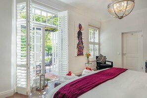 Une chambre à coucher avec un grand lit, des volets blancs, un lustre et un tableau au mur.