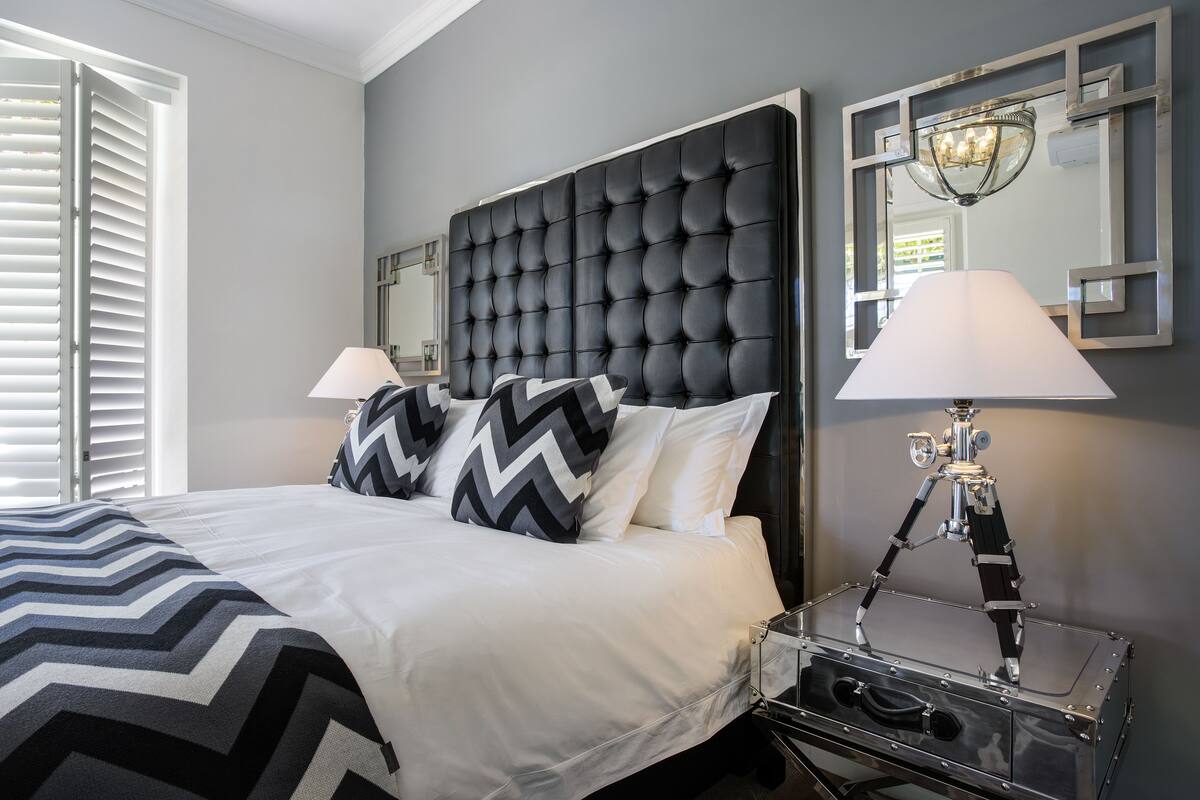 A neatly made bed with a black and white chevron-patterned bedspread, a tufted headboard, and two bedside lamps.