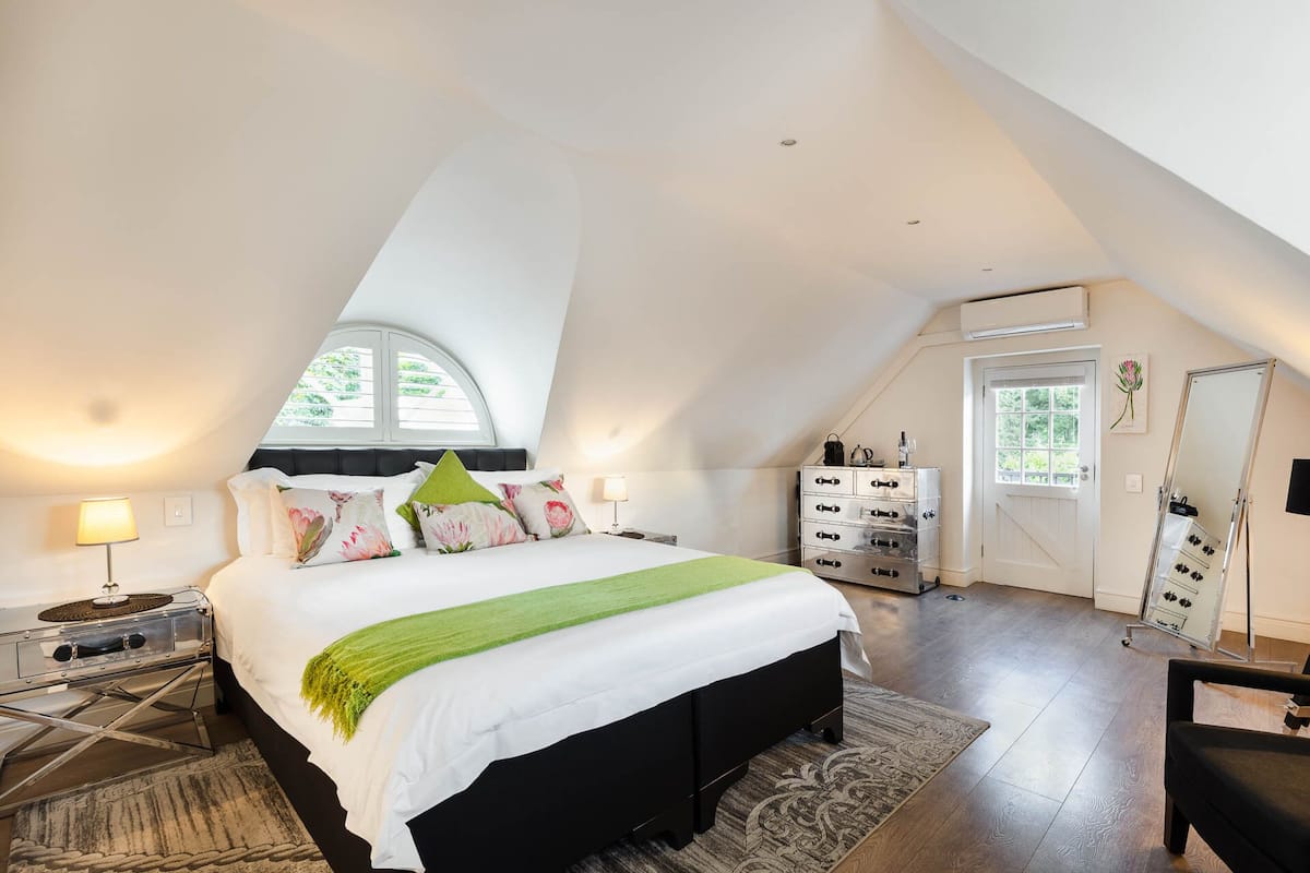 A spacious bedroom with a large bed, a dresser, a mirror, and a skylight.